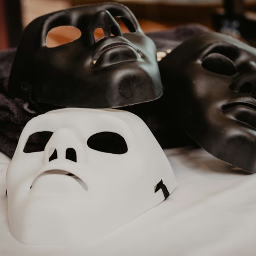 The Double Mask — two black masks and a white mask on a table
